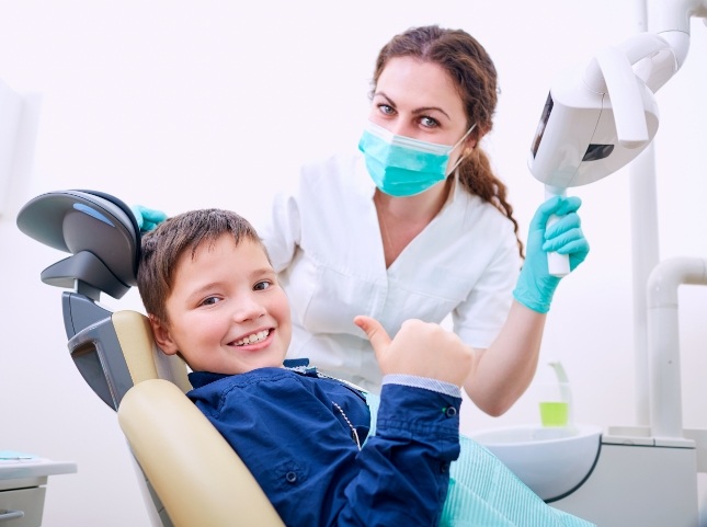 Young boy in dental chair smiling and giving a thumbs up