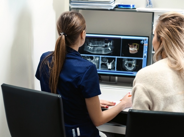 Dental team member showing a woman x rays of teeth on computer monitors