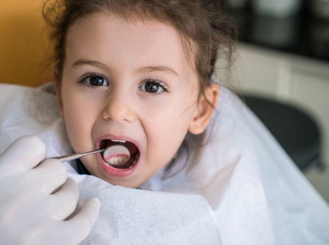 Child in dental chair with dental mirror in their mouth