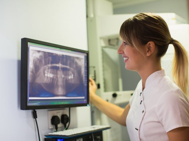 Dental team member looking at monitor showing x rays of teeth
