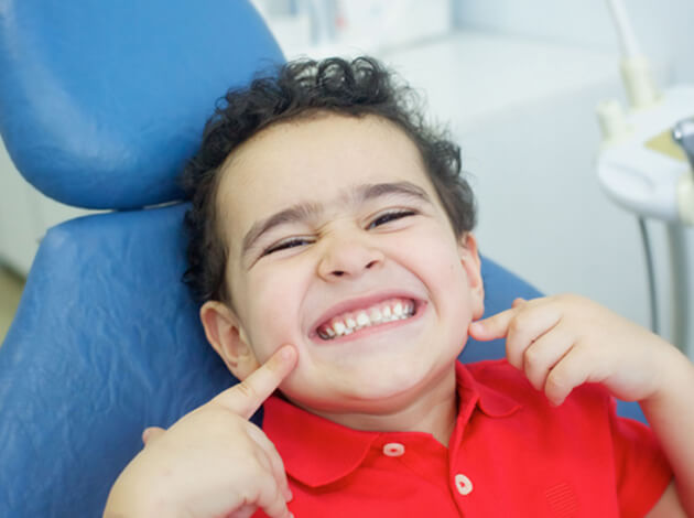 Young boy smiling and pointing at teeth  