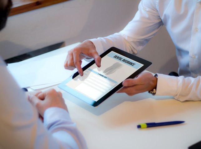 Two people sitting at desk and looking at dental insurance information on tablet