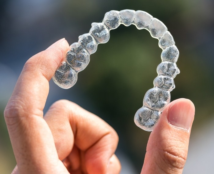 Hand holding an Invisalign aligner outdoors