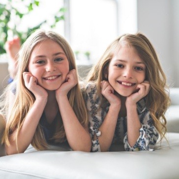 Two smiling young girls laying on their stomachs on carpet