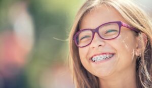 Girl with purple glasses outside smiling with braces